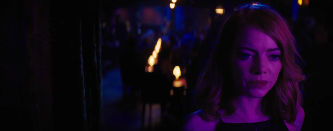 La La Land (2016) movie still: closeup — A dimly lit indoor dining space features rows of blurred tables with lit candles. A woman stands in the…