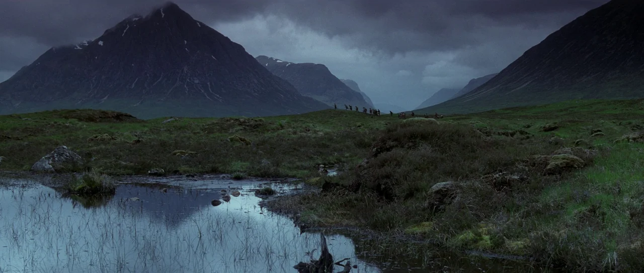 Braveheart (1995) movie still: establishing — A vast, moody Scottish highland landscape features craggy green mountains under a heavy overcast sky.…
