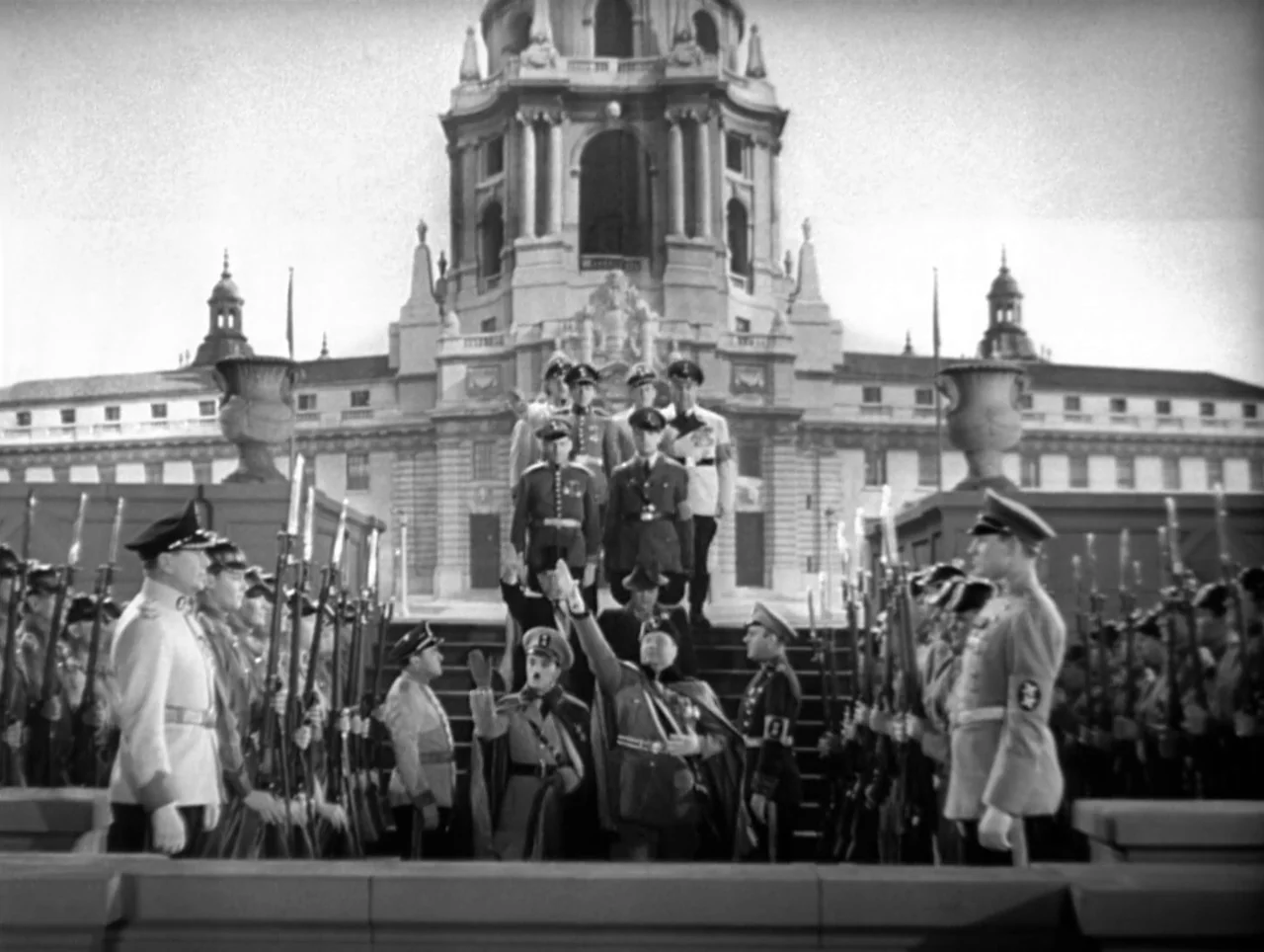 The Great Dictator (1940) movie still: wide — A grand, classical stone government building with a central dome serves as the backdrop. Soldiers in…