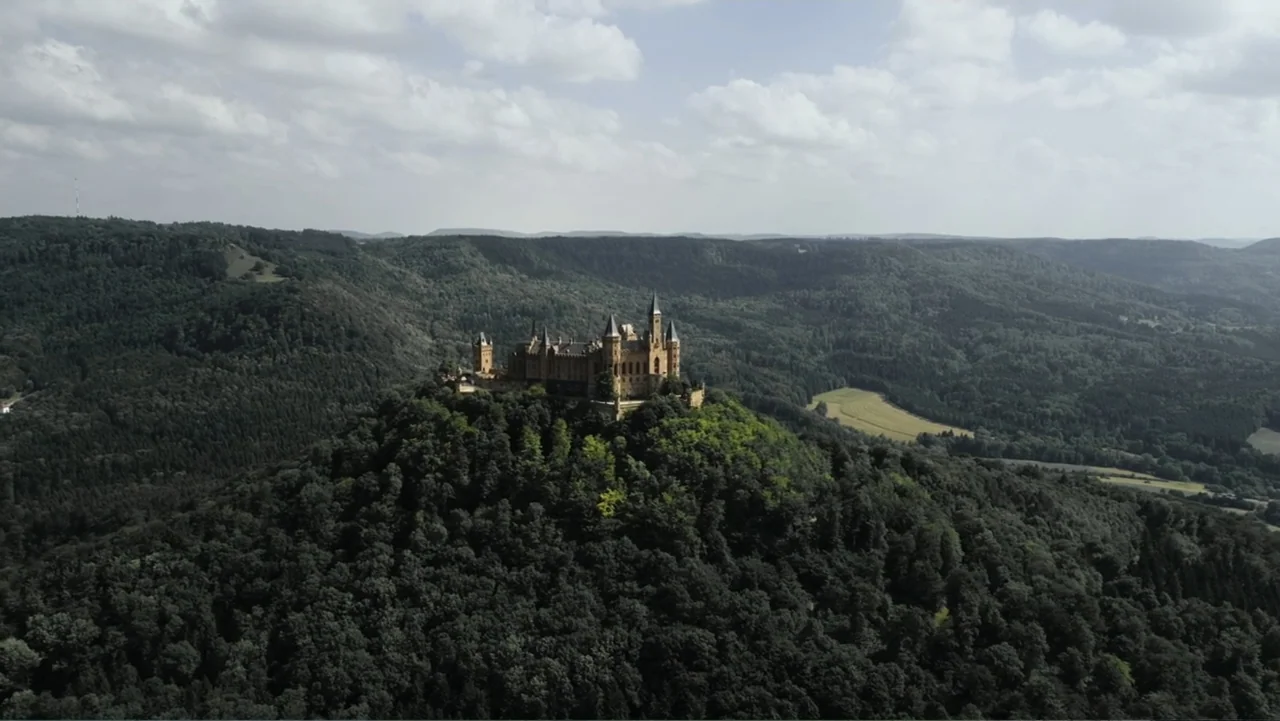 Empire Queen: The Golden Age of Magic (2024) movie still: establishing — A stone castle with multiple towers stands atop a lush, tree-covered…