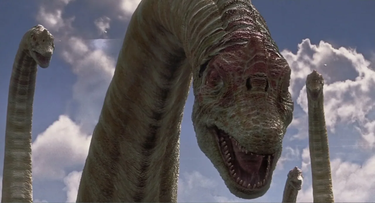 Jurassic Park III (2001) movie still: medium — Multiple long-necked sauropod dinosaurs reach their heads toward the sky in daylight. The prehistoric…