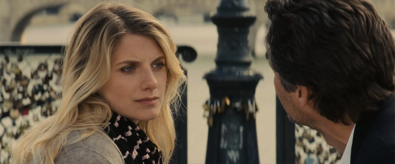 Now You See Me (2013) movie still: medium — A metal bridge railing covered in small padlocks stands in an urban setting. A blonde woman faces a man…