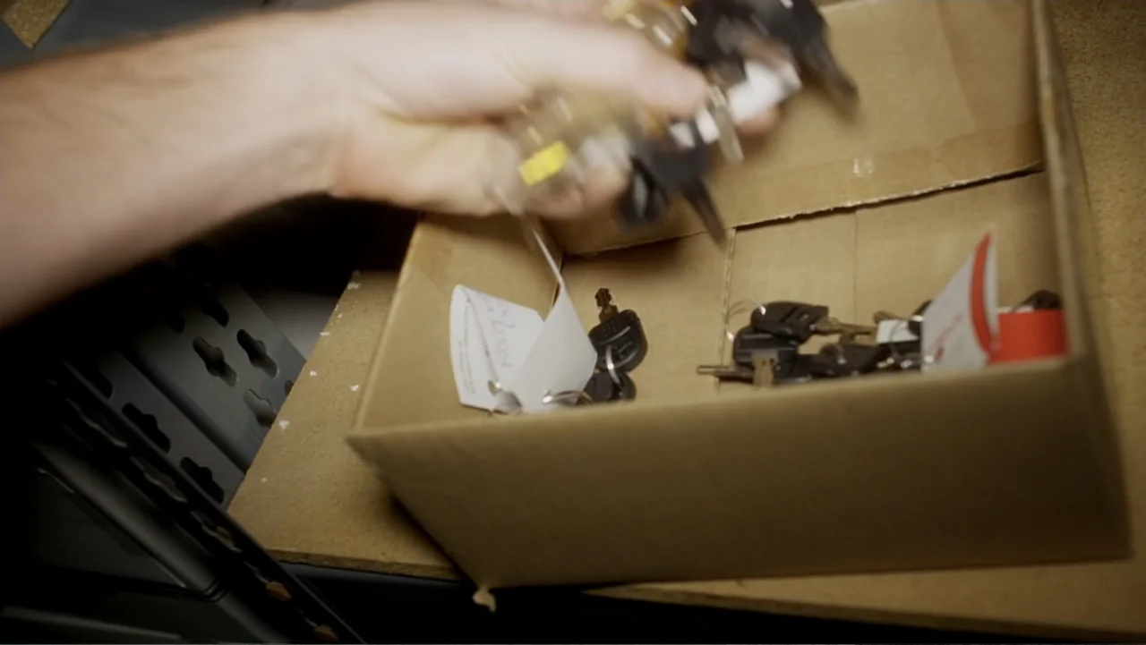 The Gallows (2015) movie still: closeup — A light brown cardboard box sits on a shelf containing several sets of keys. A hand reaches into the frame…