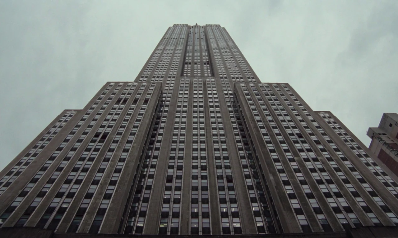 Vox Lux (2018) movie still: establishing — The Empire State Building rises vertically into an overcast, grey sky. The massive stone and glass…