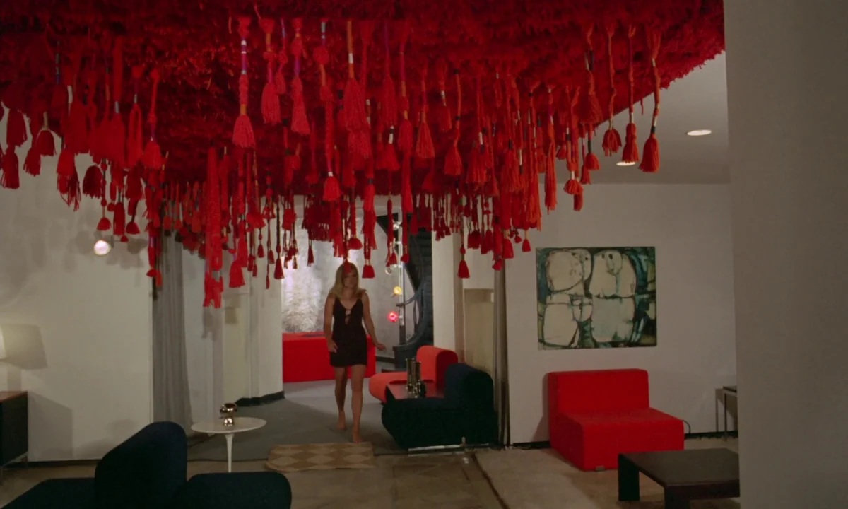 Vampyros Lesbos (1971) movie still: wide — A spacious 1970s interior features white walls adorned with abstract art and geometric furniture. A…