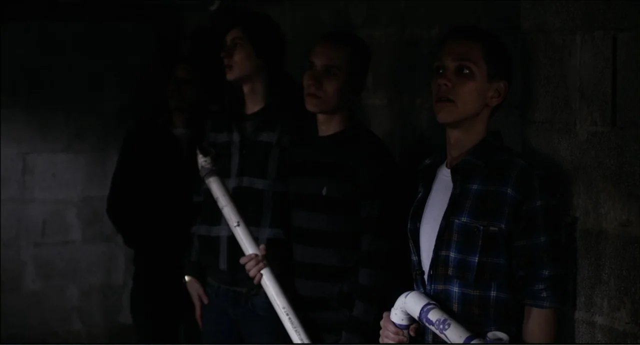The Secret Village (2013) movie still: medium — A dark basement with unfinished concrete block walls provides a dim setting for the subjects. Three…
