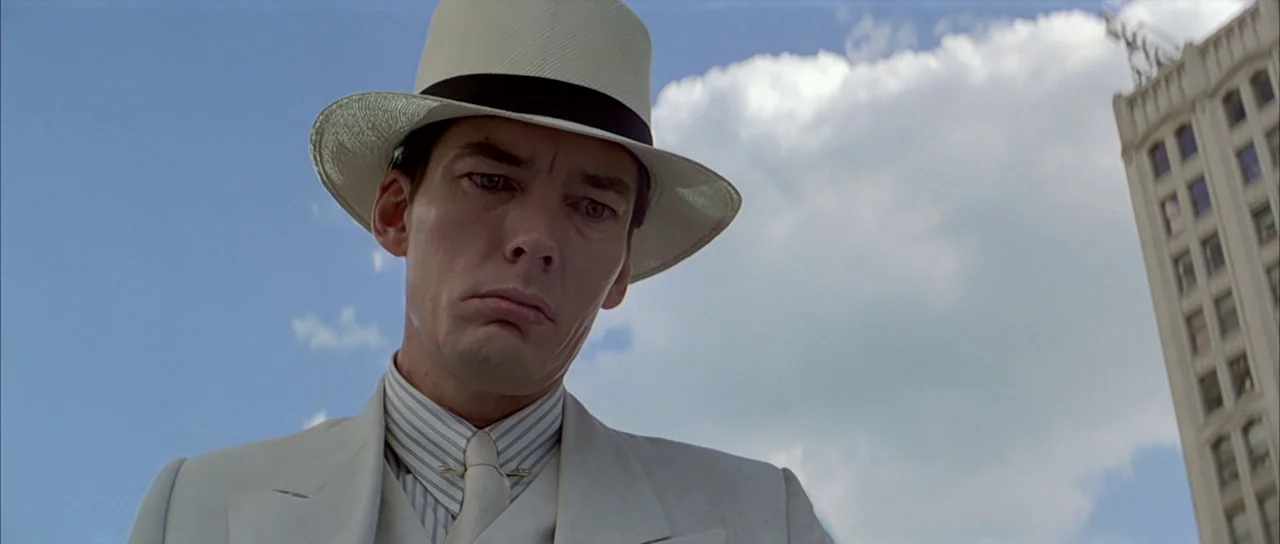 The Untouchables (1987) movie still: medium — A man stands outdoors against a bright blue sky with a large building nearby. He gazes downward while…