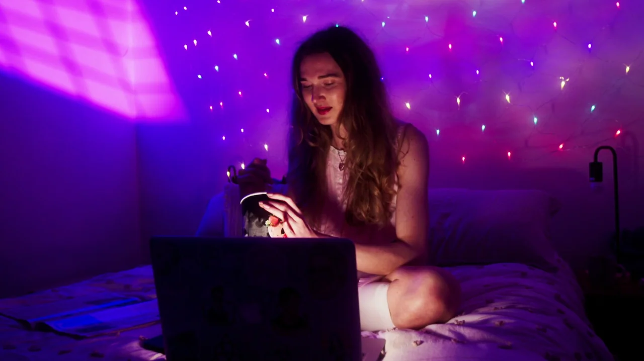 Carnage for Christmas (2024) movie still: medium — A dark bedroom decorated with glowing multi-colored string lights against the back wall. A woman…
