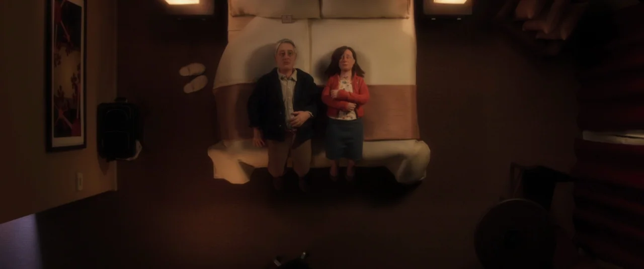 Anomalisa (2015) movie still: wide — A top-down view of a hotel room with a large unmade bed. Two stop-motion figures lie side-by-side on the bed…