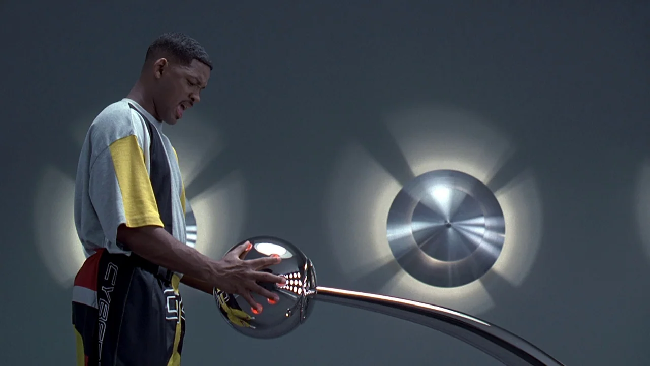 Men In Black (1997) movie still: medium — A sterile gray room features circular wall-mounted metallic fixtures that emit soft light. A young man…