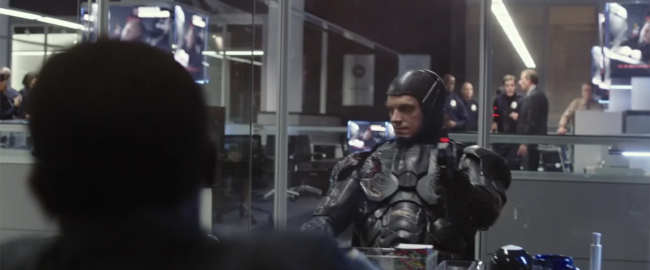 RoboCop (1987) movie still: medium — A modern police department office features glass partitions and monitors displaying digital data. A cybernetic…