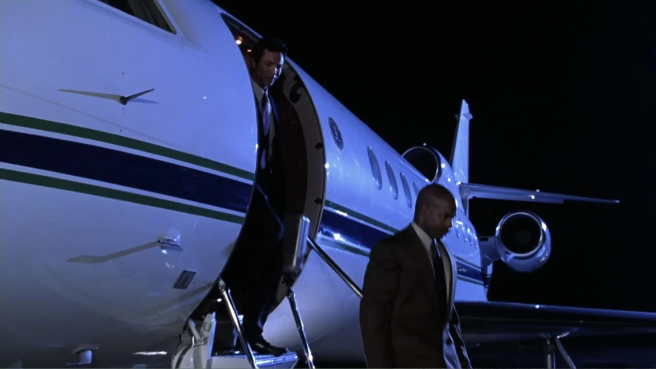 Miss Congeniality (2000) movie still: fullbody — A private jet sits on a dark tarmac at night with the stairs deployed. Two men in business suits…