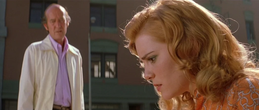 Where The Truth Lies (2005) movie still: medium — A woman stands in the foreground with an older man positioned slightly behind her. An urban…