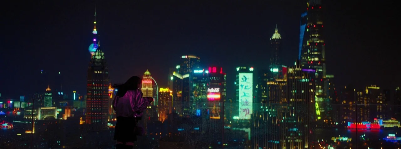 Dead Pigs (2018) movie still: wide — A dark, elevated rooftop balcony overlooks a sprawling modern city skyline at night. A young woman in a…