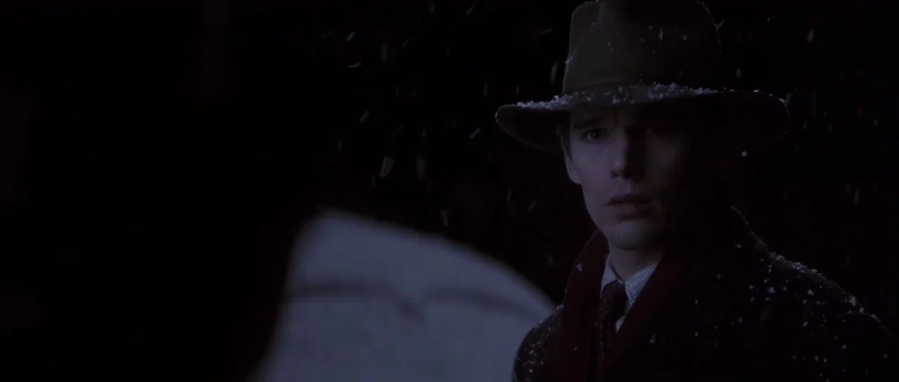 Snow Falling on Cedars (1999) movie still: medium — A man in a hat stands outside at night as light snow falls around him. He is looking off-camera…
