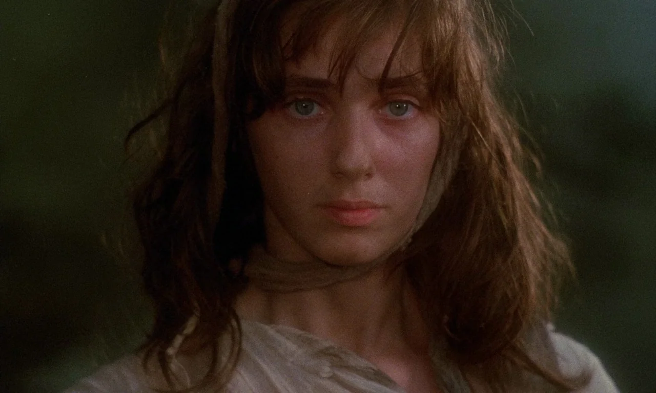 The Church (1989) movie still: closeup — An outdoor natural setting with blurred green foliage in the background. A young woman with messy hair…