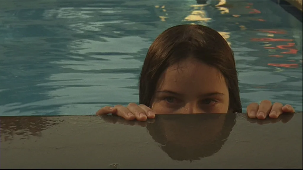 Margot At The Wedding (2007) movie still: closeup — A teenage girl is submerged in a swimming pool up to her eyes. She rests her hands on the edge…