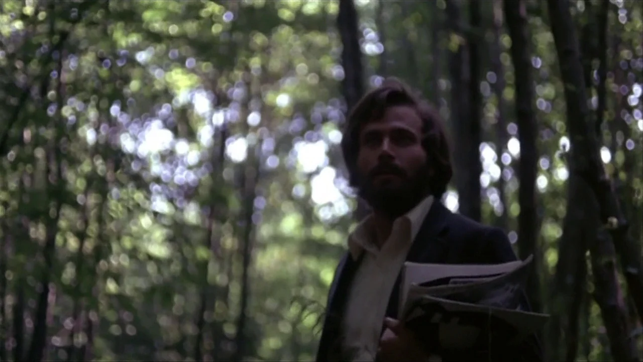 A Quiet Place In The Country (1968) movie still: medium — A man stands in a thick forest with dappled light hitting the surrounding trees. He holds…