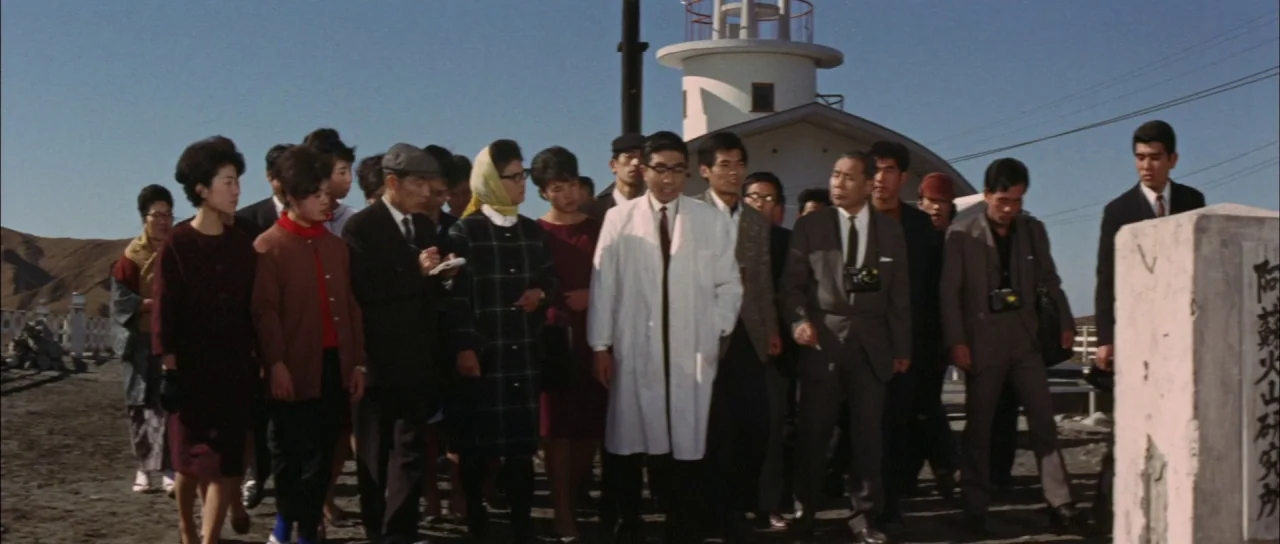 Ghidorah The Three Headed Monster (1964) movie still: fullbody — A group of people walk past a white stone pillar on a dusty path. A small…