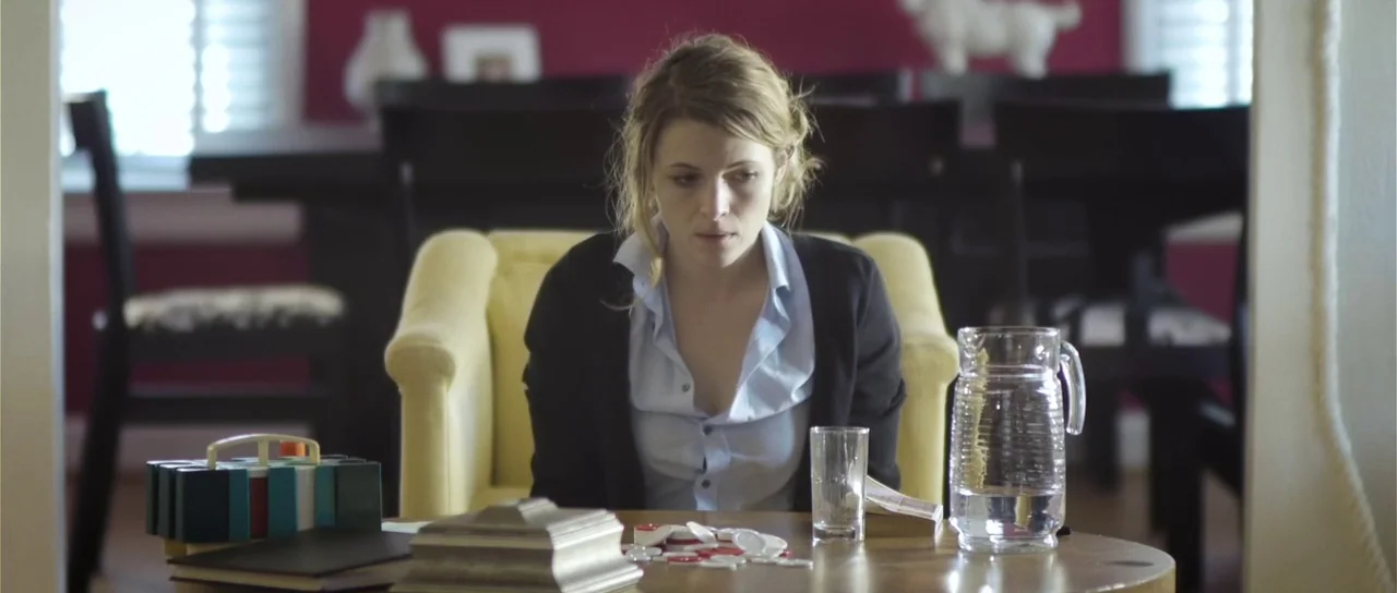 Upstream Color (2013) movie still: medium — A bright room features a round wooden table with a magenta wall behind it. A woman in a light blue shirt…