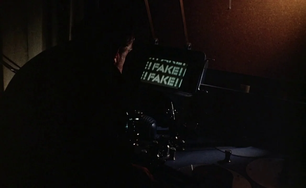 F for Fake (1973) movie still: medium — A dark editing room features a vintage film splicing machine with illuminated screen text. A person sits at…