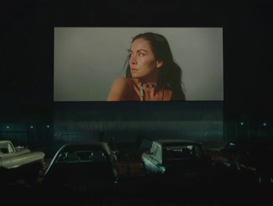 The Other Side of the Wind (2018) movie still: wide — A dark outdoor lot filled with parked cars faces a large illuminated cinema screen. The screen…