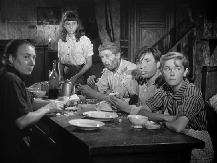 Forbidden Games (1952) movie still: medium — A rustic interior scene shows a group of five people seated at a wooden table. They are gathered for a…