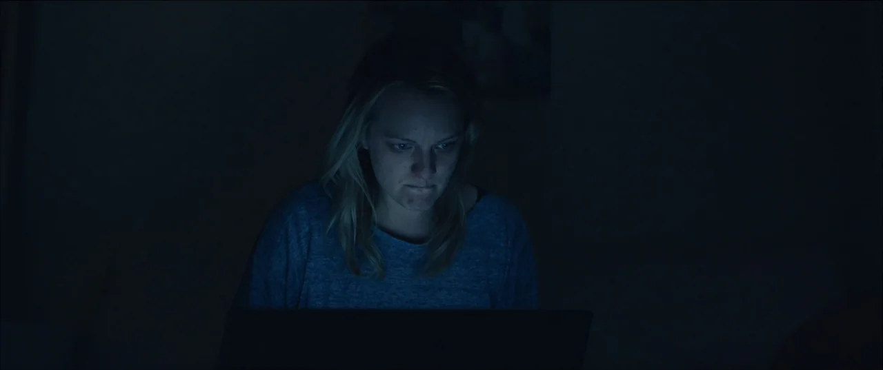 The Invisible Man (2020) (2020) movie still: medium — A woman sits in a dark bedroom at night. She is illuminated by the light of a laptop screen.