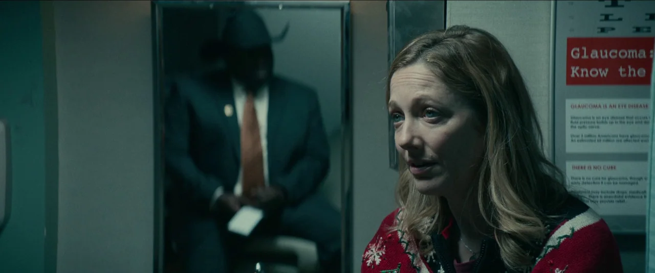 Halloween Kills (2021) movie still: medium — A clinical office room features a framed medical chart on the wall. A woman in a festive sweater sits…