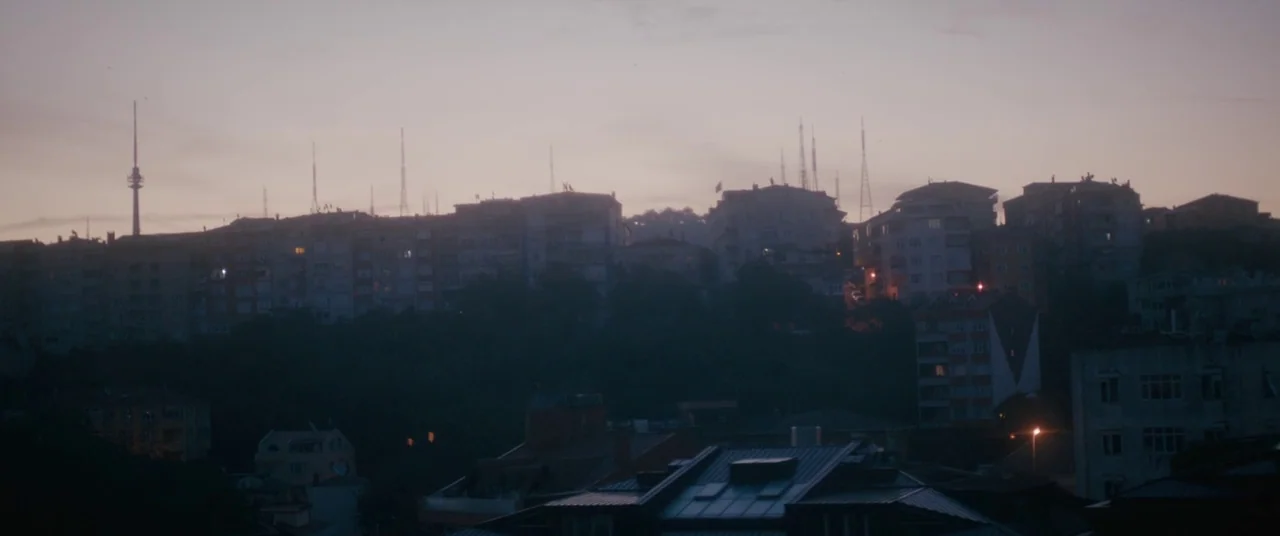 Mustang (2015) movie still: establishing — A dense urban residential area sits atop a hill at twilight with scattered windows glowing. Numerous…