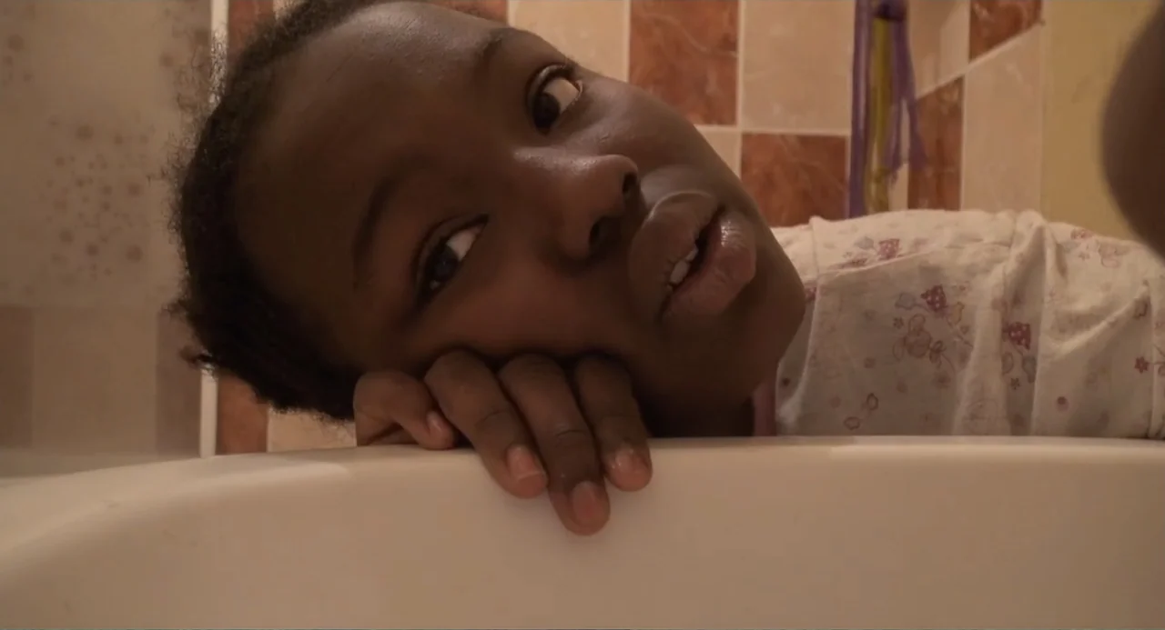 A Dramatic Film (2019) movie still: closeup — A tiled bathroom features a light-colored surface in the foreground of the frame. A young person rests…