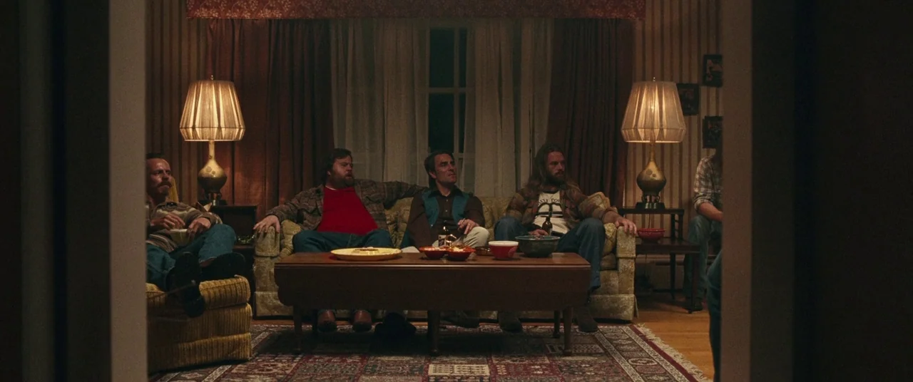BlacKkKlansman (2018) movie still: wide — A dimly lit room with 1970s floral wallpaper and matching furniture. Four men sit on a couch and an…