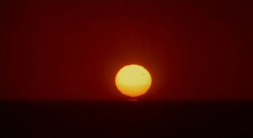 Mishima: A Life in Four Chapters (1985) movie still: establishing — A deep red horizon line meets the dark sky at sunset over the ocean. The bright…