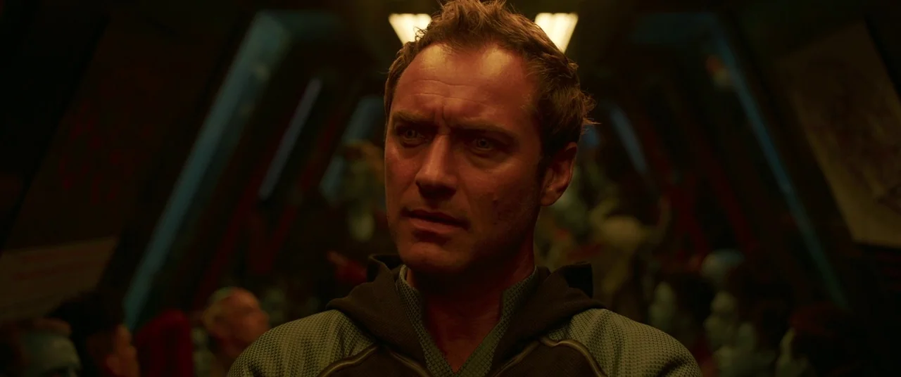 Captain Marvel (2019) movie still: closeup — A dark corridor inside a futuristic vessel features angled walls and overhead light fixtures. A man…