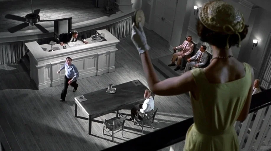 Pleasantville (1998) movie still: wide — A high-angle view looking down into a large, formal hall with wooden flooring. A woman in a dress observes…