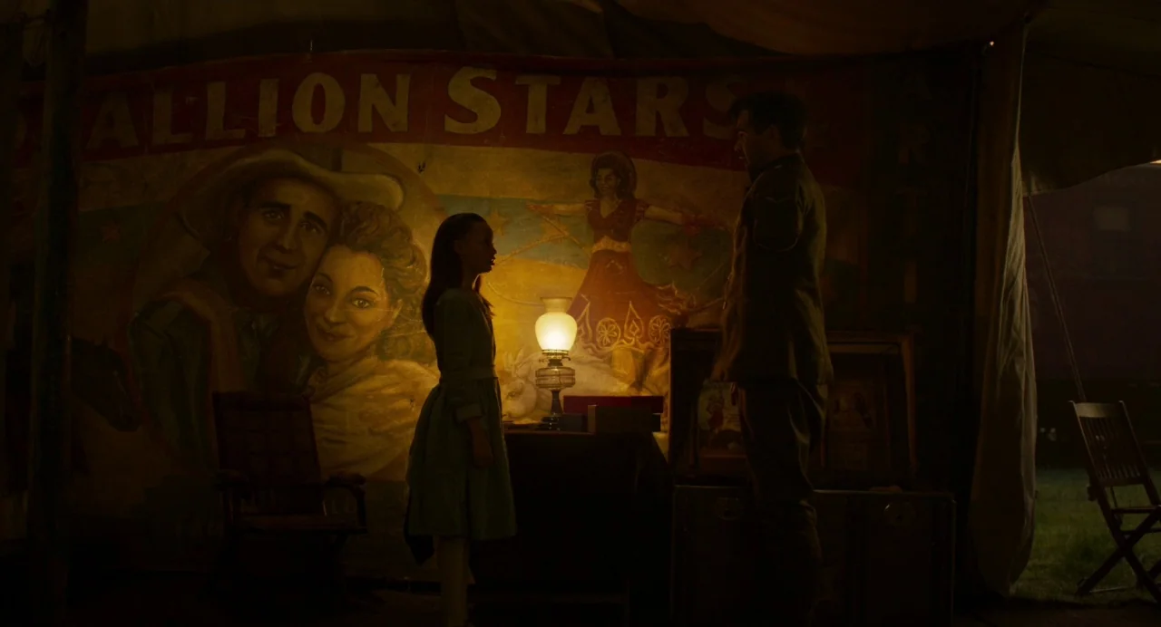 Dumbo (2019) movie still: medium — A large canvas tent features a painted mural of circus stars in the background. A young girl and a man in a…