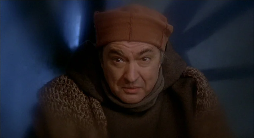 Quintet (1979) movie still: closeup — A dimly lit, dark space with a person wearing a brown monk's hood. The man is looking directly ahead towards…
