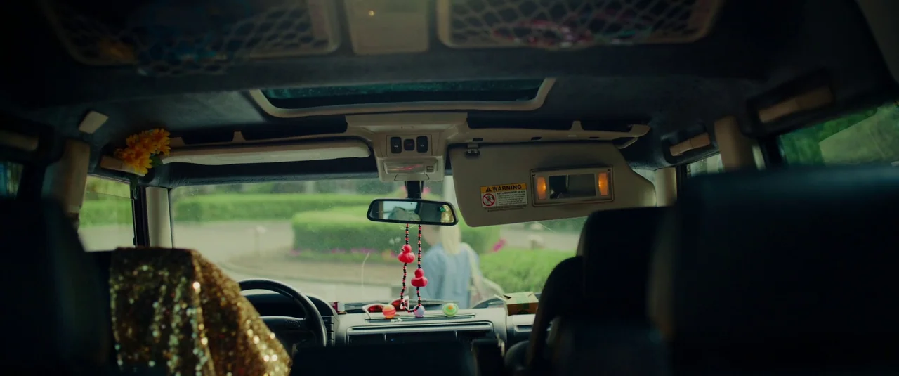 Bodies Bodies Bodies (2022) movie still: wide — The view from inside a car looking out through the front windshield at greenery. A person walks…