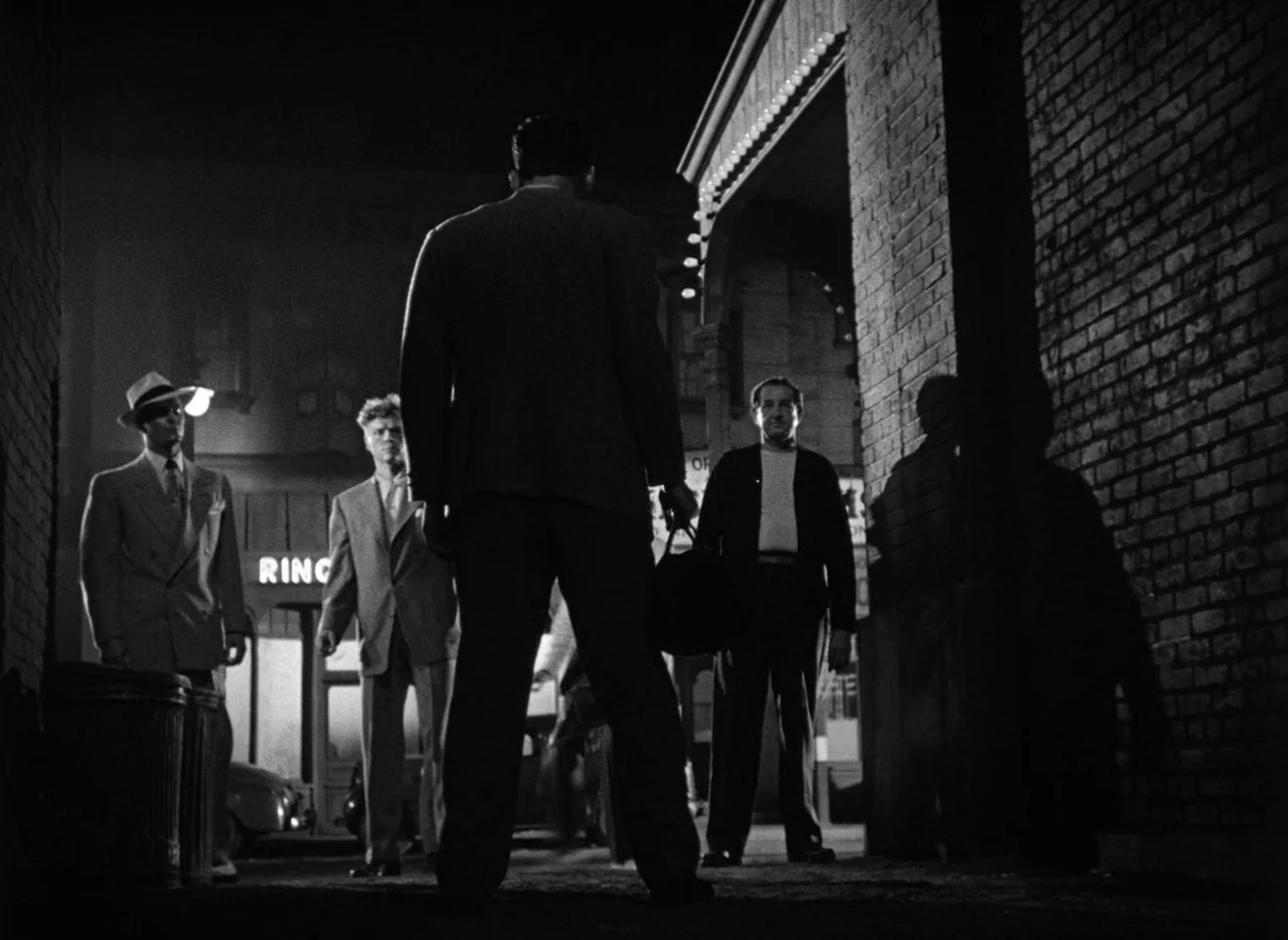 The Set-Up (1949) movie still: fullbody — A dark urban alleyway features a brick wall and a street lamp overhead. A man in a suit confronts three…