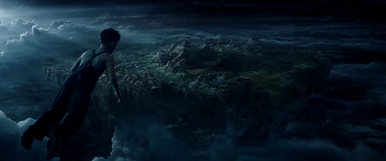 Pan (2015) movie still: wide — A dark, atmospheric landscape features a large, jagged rock island suspended in the night sky. A young boy in…