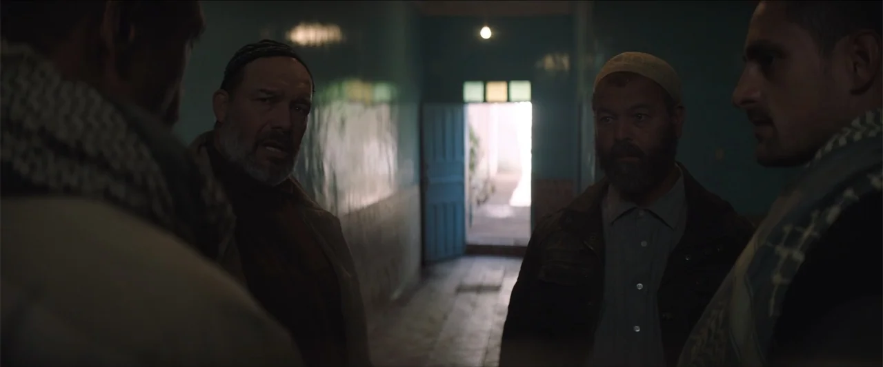 Redemption Day (2021) movie still: medium — A dimly lit indoor corridor with tiled walls leads to a brightly lit open doorway. Four men stand in a…