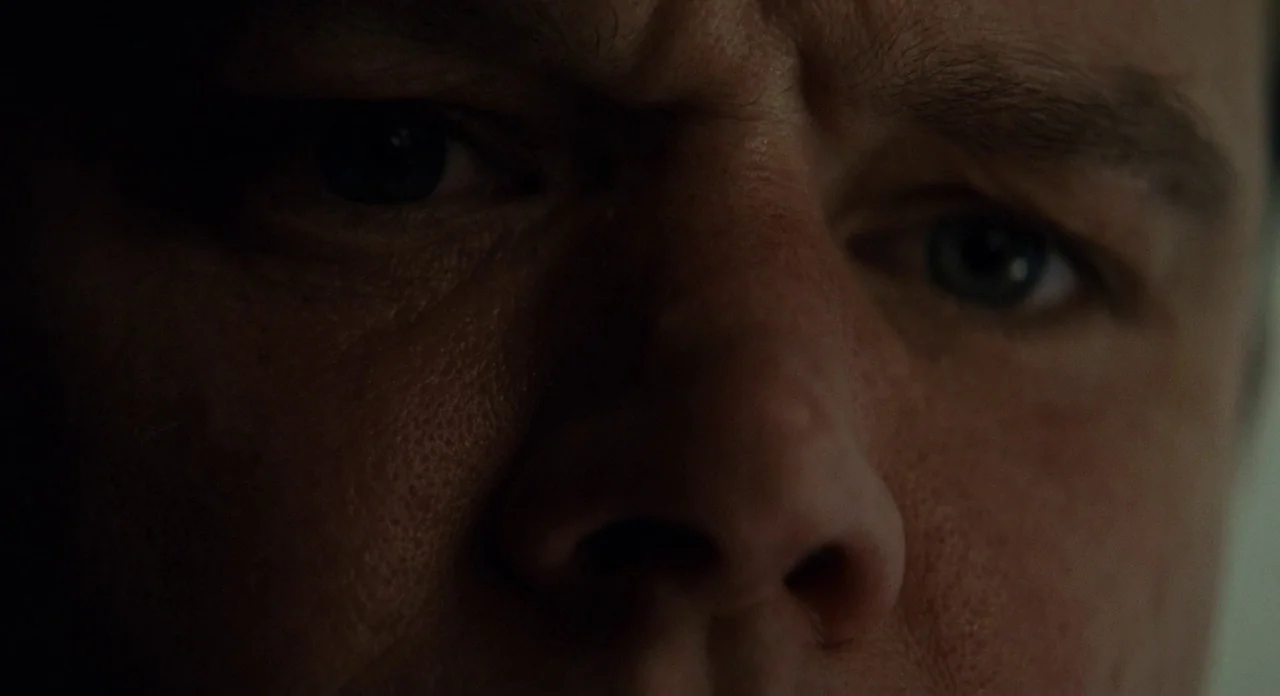 Promised Land (2012) movie still: closeup — A close-up view focuses on the weathered face of a middle-aged man. The man stares forward with a…