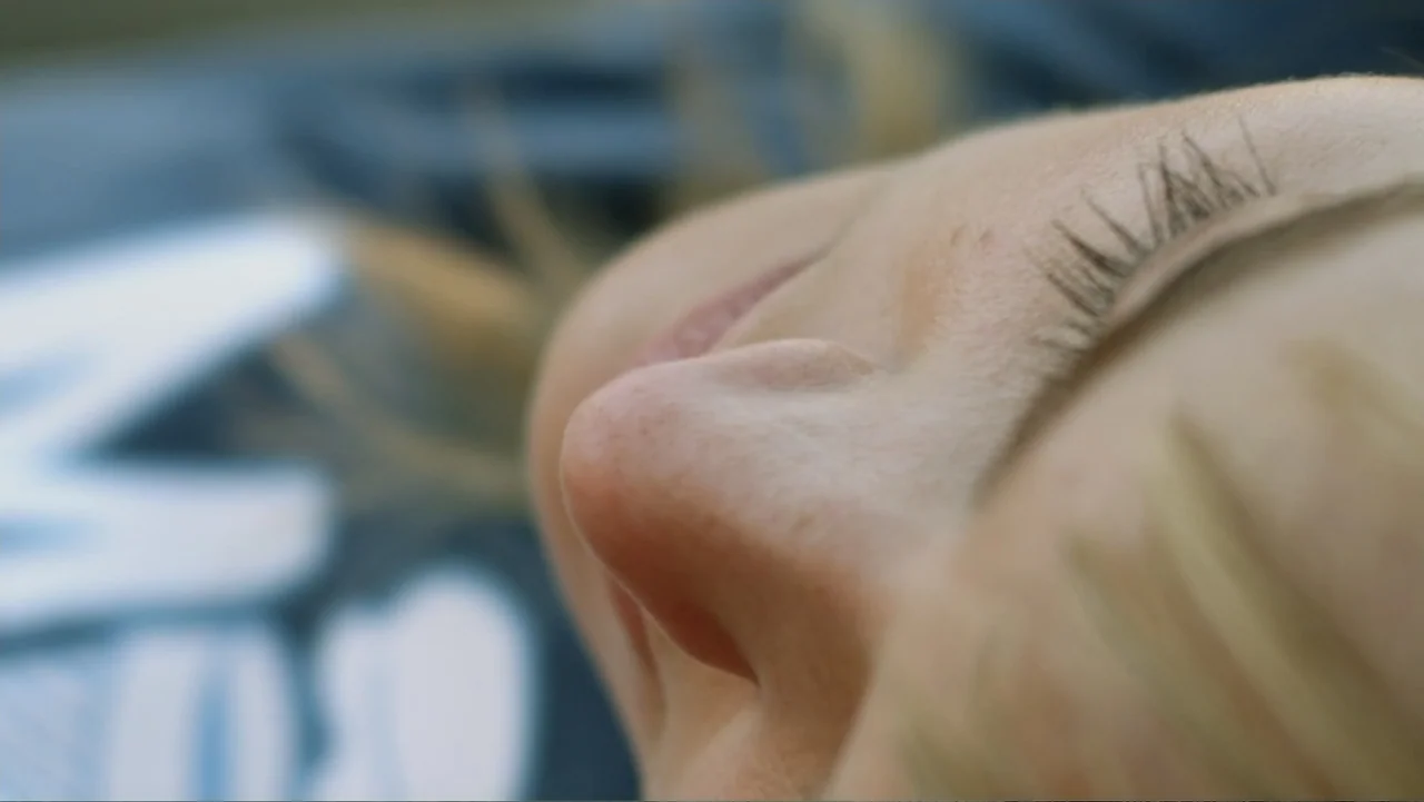 Free Samples (2013) movie still: closeup — A close view of a person lying down against a dark fabric background. The subject is oriented in profile…