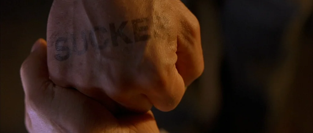 The Underneath (1995) movie still: closeup — A close-up shot focuses on the back of a male hand. The letters S-U-C-K-E-R are tattooed across the…