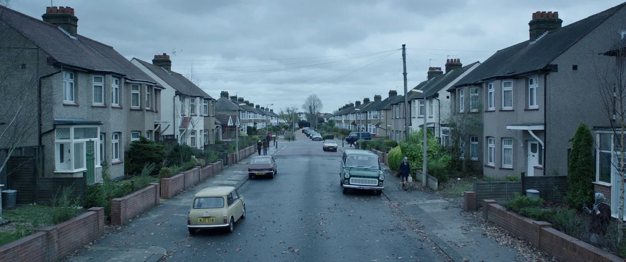 The Conjuring 2 (2016) movie still: establishing — A quiet British suburban street is lined with identical two-story brick houses under grey skies.…