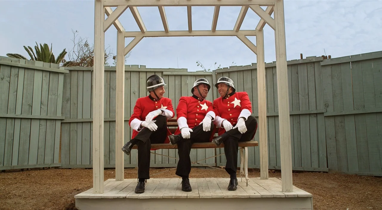 Dance of Reality (2013) movie still: fullbody — A light-colored wooden trellis structure encloses a bench in a fenced-in sandy area. Three men in…