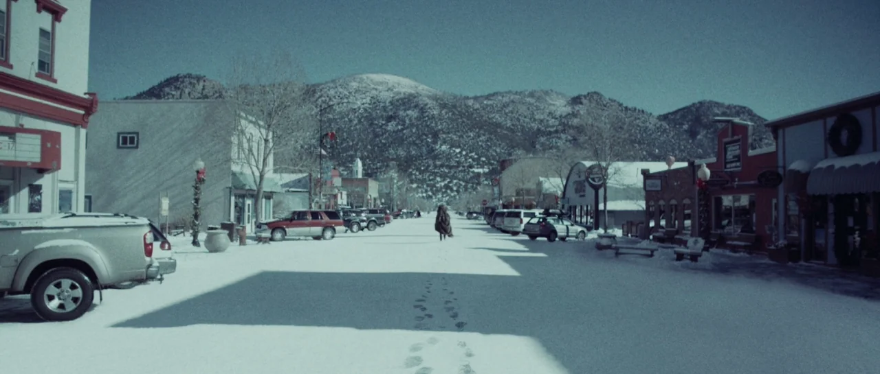 Starfish (2018) movie still: establishing — A snow-covered town street is framed by small commercial buildings and mountain peaks. A single person…