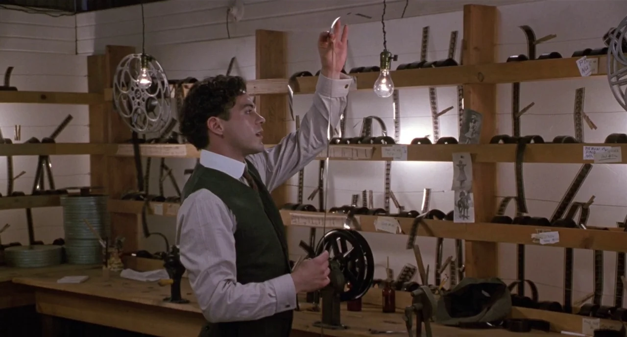 Chaplin (1992) movie still: medium — A workspace features tiered wooden shelves filled with organized canisters and exposed film strips. A young man…