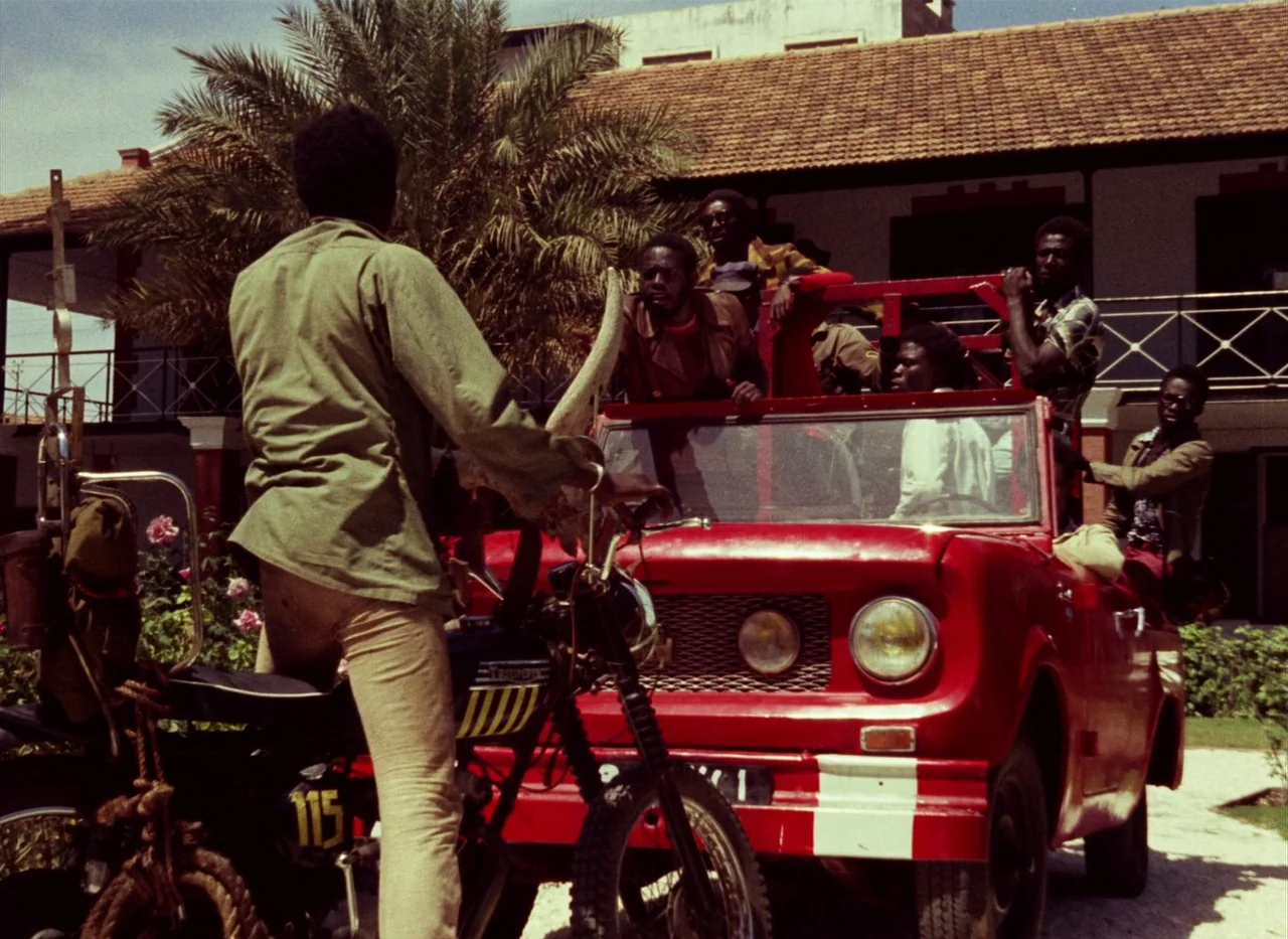 Touki Bouki (1973) movie still: fullbody — A man on a motorcycle stops before a red jeep parked in a driveway. The group of men inside the jeep…