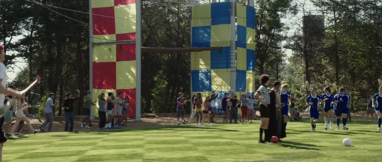 The Internship (2013) movie still: wide — An open green sports field features large checkered red and blue towers in the background. A crowd of…